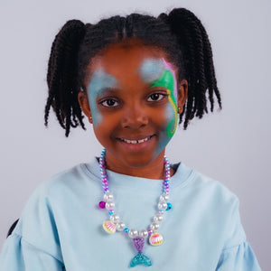 Step one, Dabbing sparkle turquoise on both sides of the face with a sponge, then painting a seahorse shape with bright green on one side, filling it in, adding ochre yellow to the belly, and bright pink to the mane.